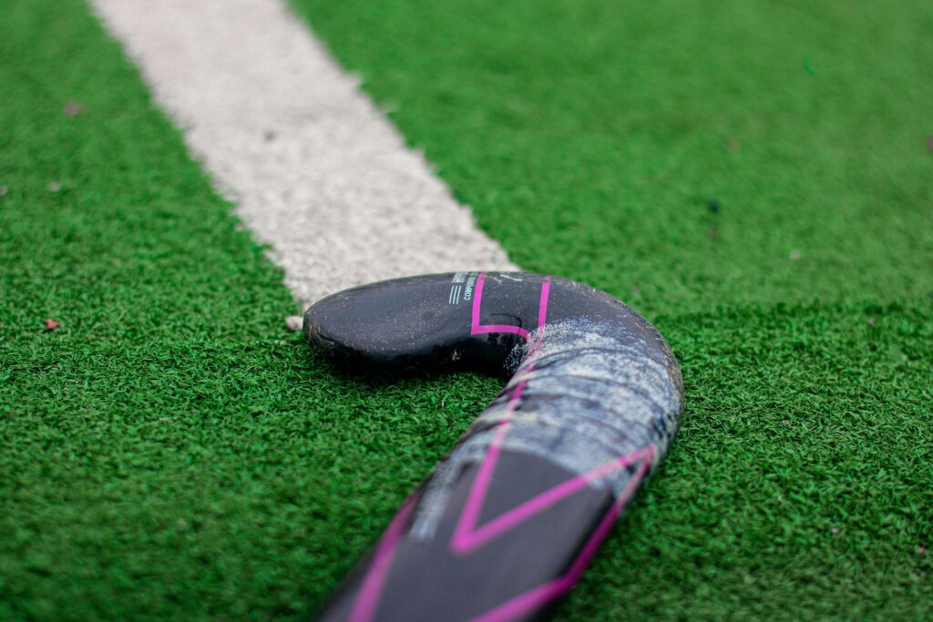 Detailed view of a field hockey stick on green artificial turf with white line.